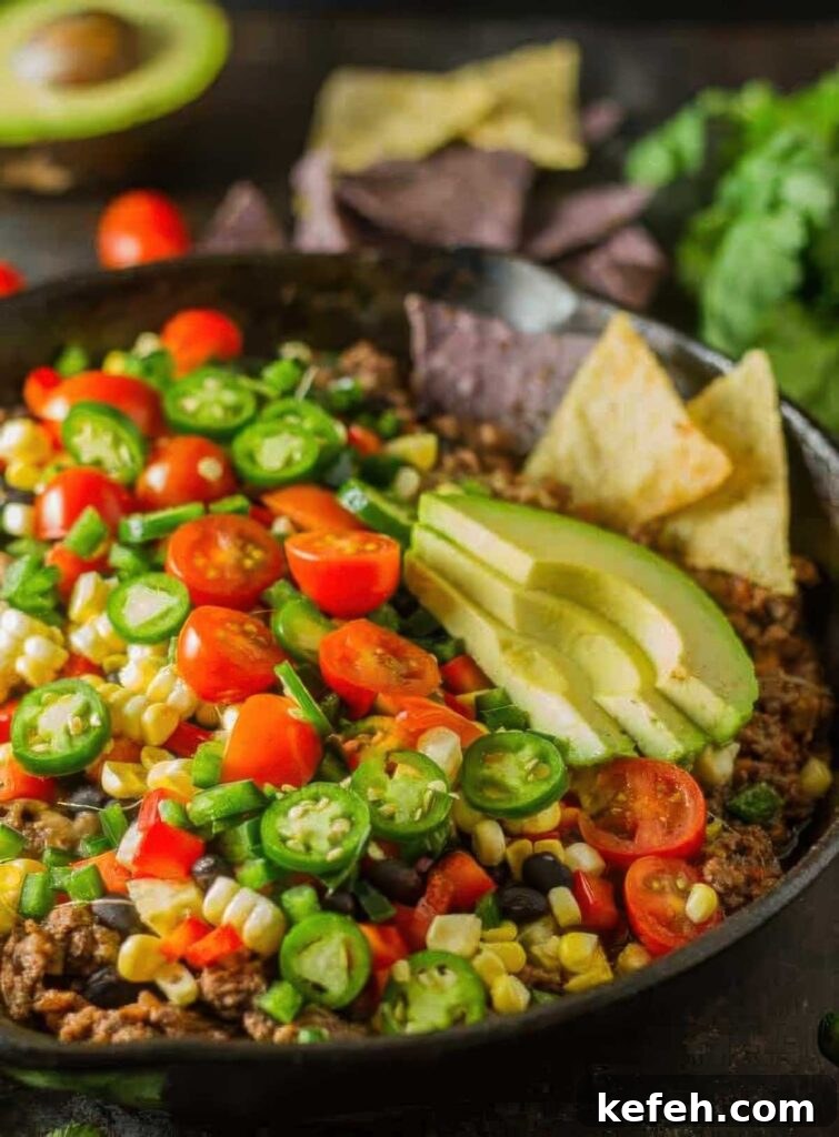Crave-Worthy Quick Nachos: Customizable Recipes for Any Meal 2 Close-up of a colorful skillet filled with healthy nachos topped with sliced avocado, cherry tomatoes, jalapeños, corn, black beans, and ground beef, served with tortilla chips.