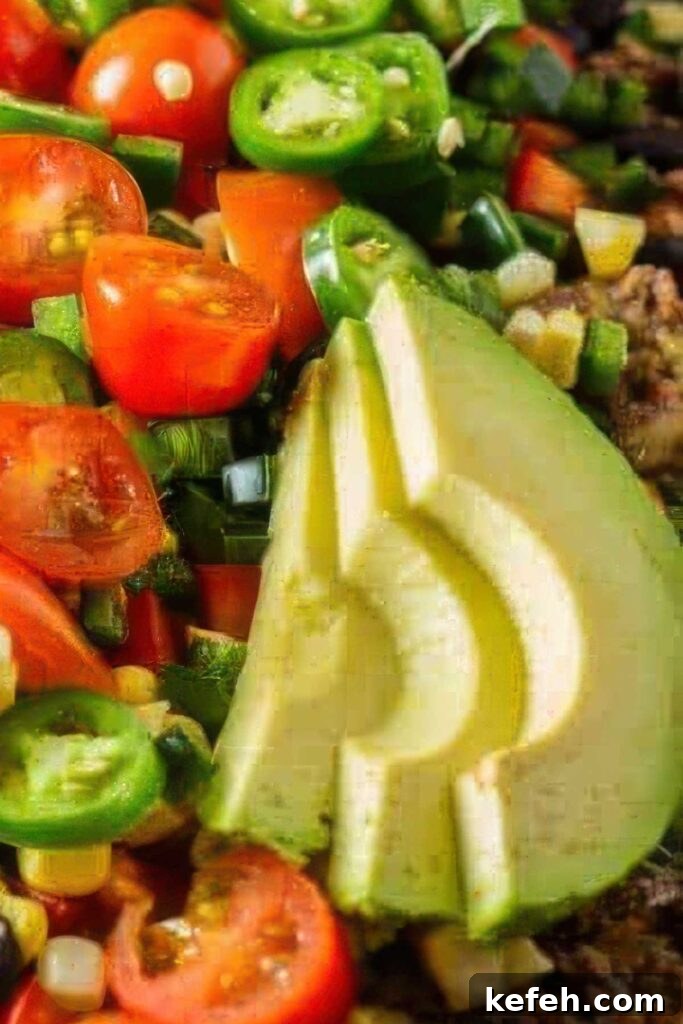 Crave-Worthy Quick Nachos: Customizable Recipes for Any Meal 4 Extreme close-up of fresh avocado slices surrounded by chopped cherry tomatoes, jalapeños, green onions, and corn atop loaded healthy nachos.