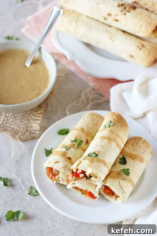 Filled with colorful veggies, cashews and fresh ginger, these baked Thai vegetable taquitos are a family favorite! Served with an orange peanut sauce for dipping! A white plate with several Vegetable Taquitos torn in half with peanut sauce to the side.