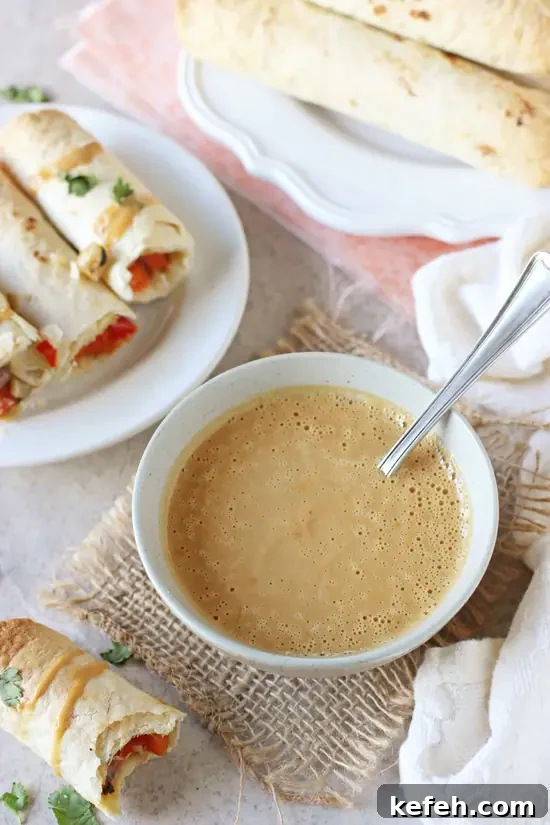 Filled with colorful veggies, cashews and fresh ginger, these baked Thai vegetable taquitos are a family favorite! Served with an orange peanut sauce for dipping! A grey bowl filled with homemade orange peanut sauce and taquitos in the background.