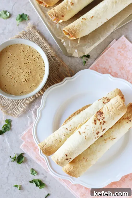 Filled with colorful veggies, cashews and fresh ginger, these baked Thai vegetable taquitos are a family favorite! Served with an orange peanut sauce for dipping! Overhead view of Thai Vegetable Taquitos on a plate with a bowl of peanut sauce to the side.