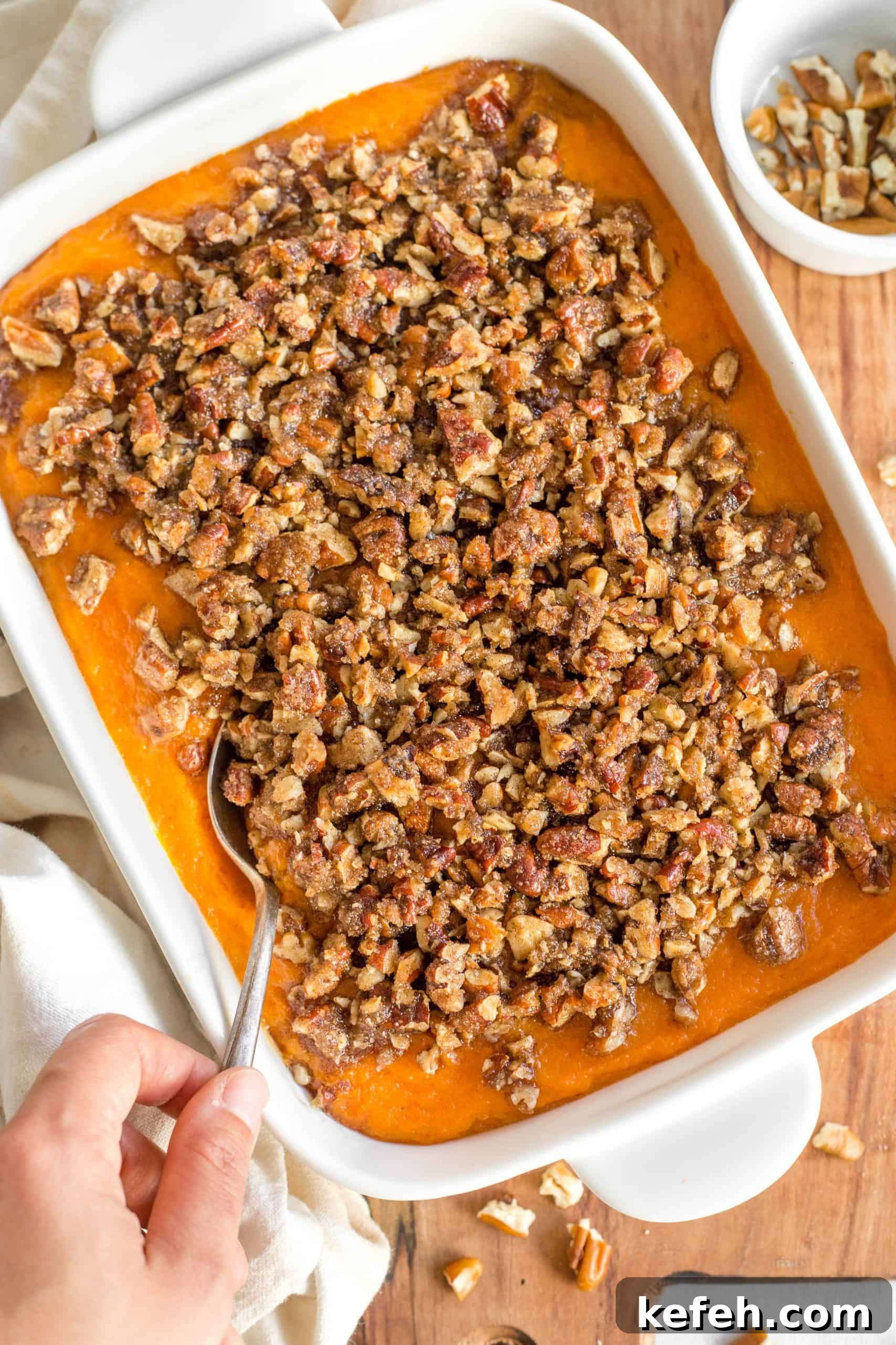 Sweet Potato Casserole (Gluten-Free, Dairy-Free) Hand holding a spoon in the casserole dish.