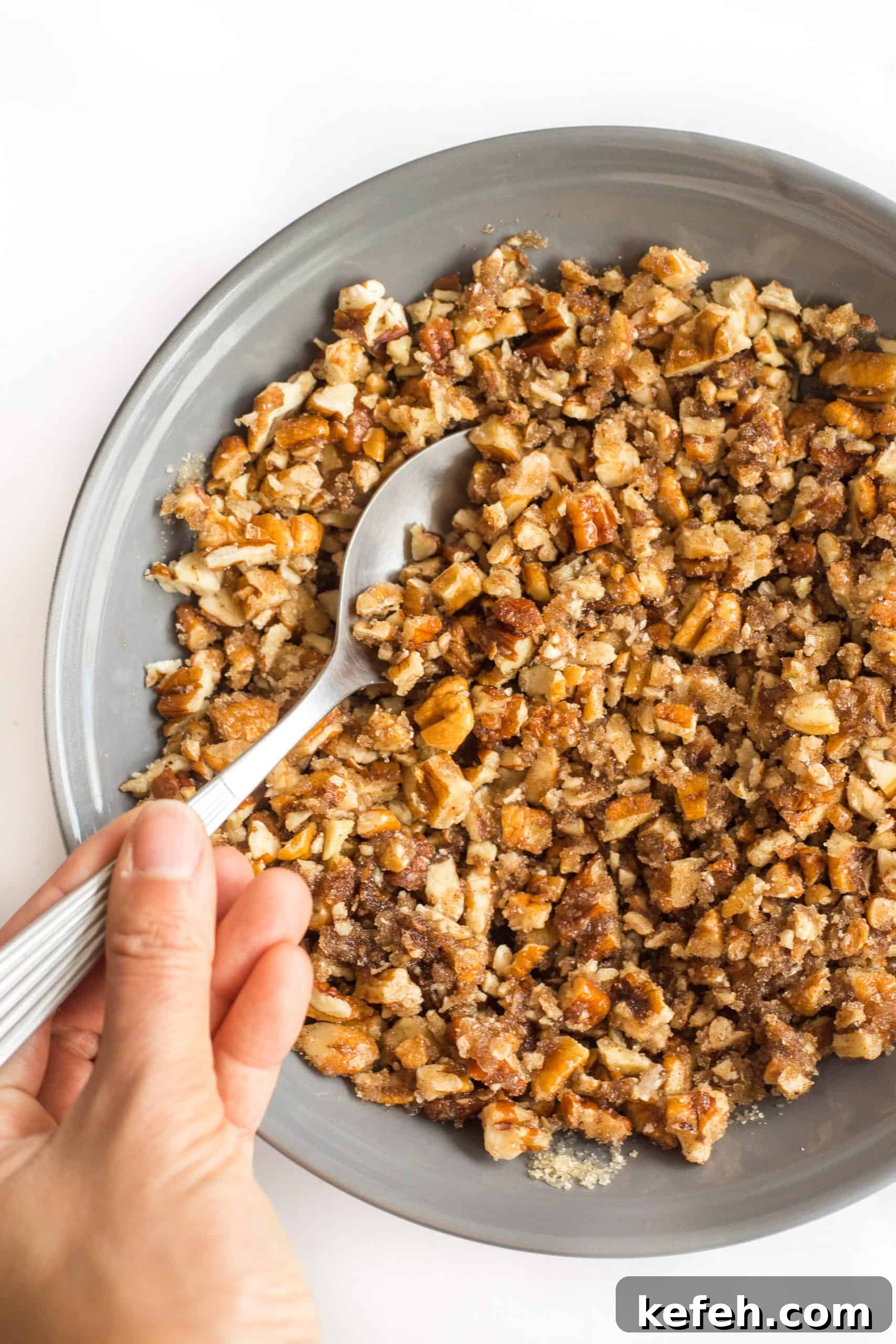 Gluten Dairy-Free Sweet Potato Casserole Hand mixing chopped pecans in a grey bowl.