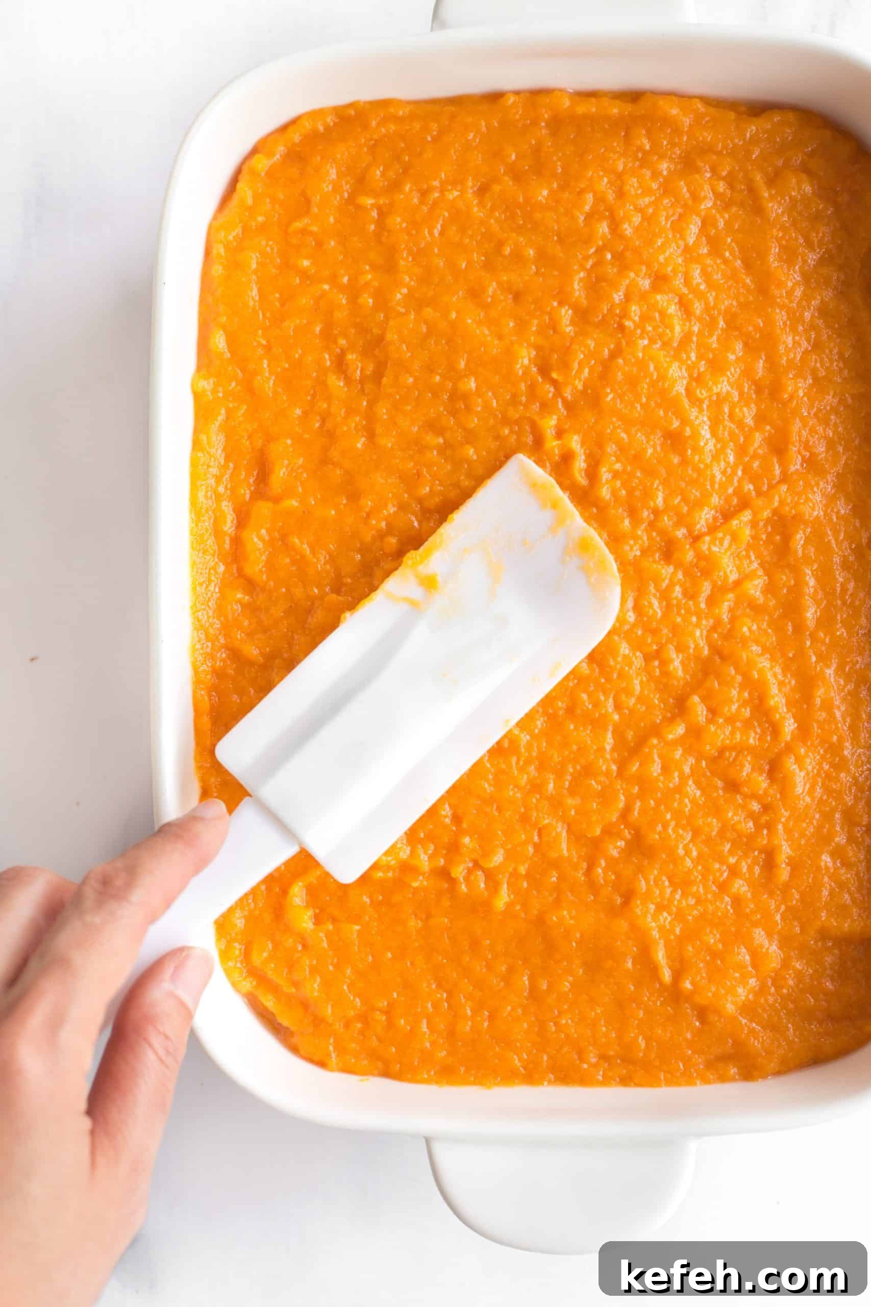 Sweet Potato Casserole Recipe (Gluten-Free, Dairy-Free) Smoothing out sweet potato filling with a spatula in a white casserole dish.