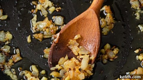 Mixed Vegetable Curry Recipe: Flavorful Indian Veggie Stew 11 Sauteed onions with garlic and ginger in a black pan with a wooden spoon
