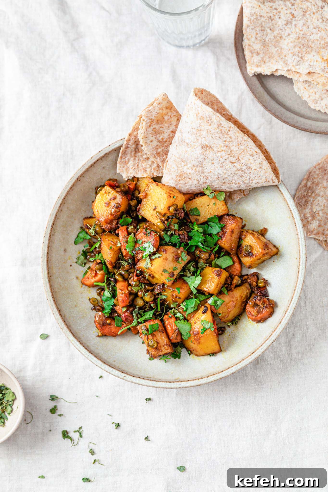 Mixed Vegetable Curry Recipe: Flavorful Indian Veggie Stew 3 Mixed vegetable curry with potatoes, carrots, and peas topped with cilantro in a beige bowl next a small bowl of methi (dried fenugreek).