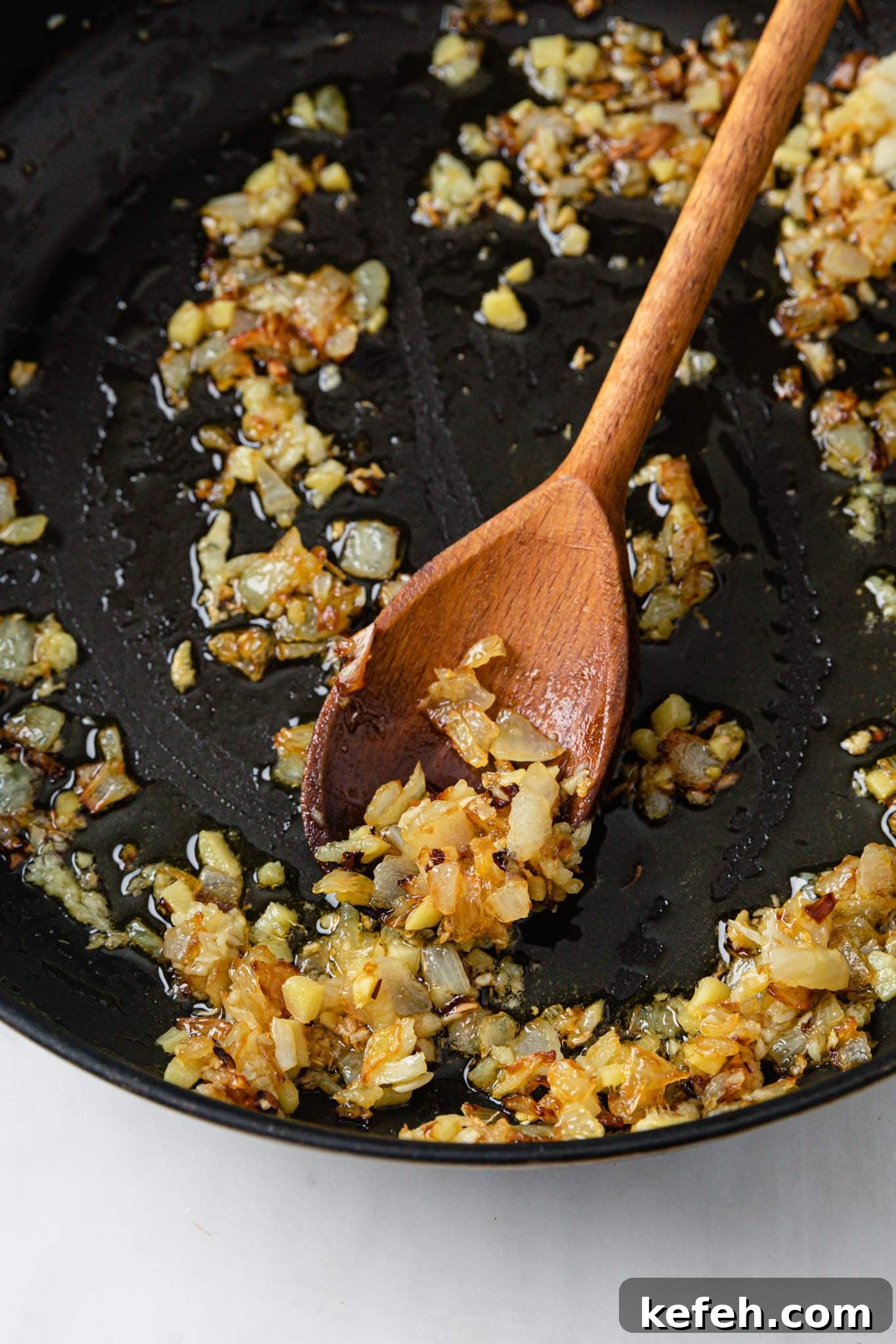 Mixed Vegetable Curry Recipe: Flavorful Indian Veggie Stew 5 Sauteed onions with garlic and ginger in a black pan with a wooden spoon