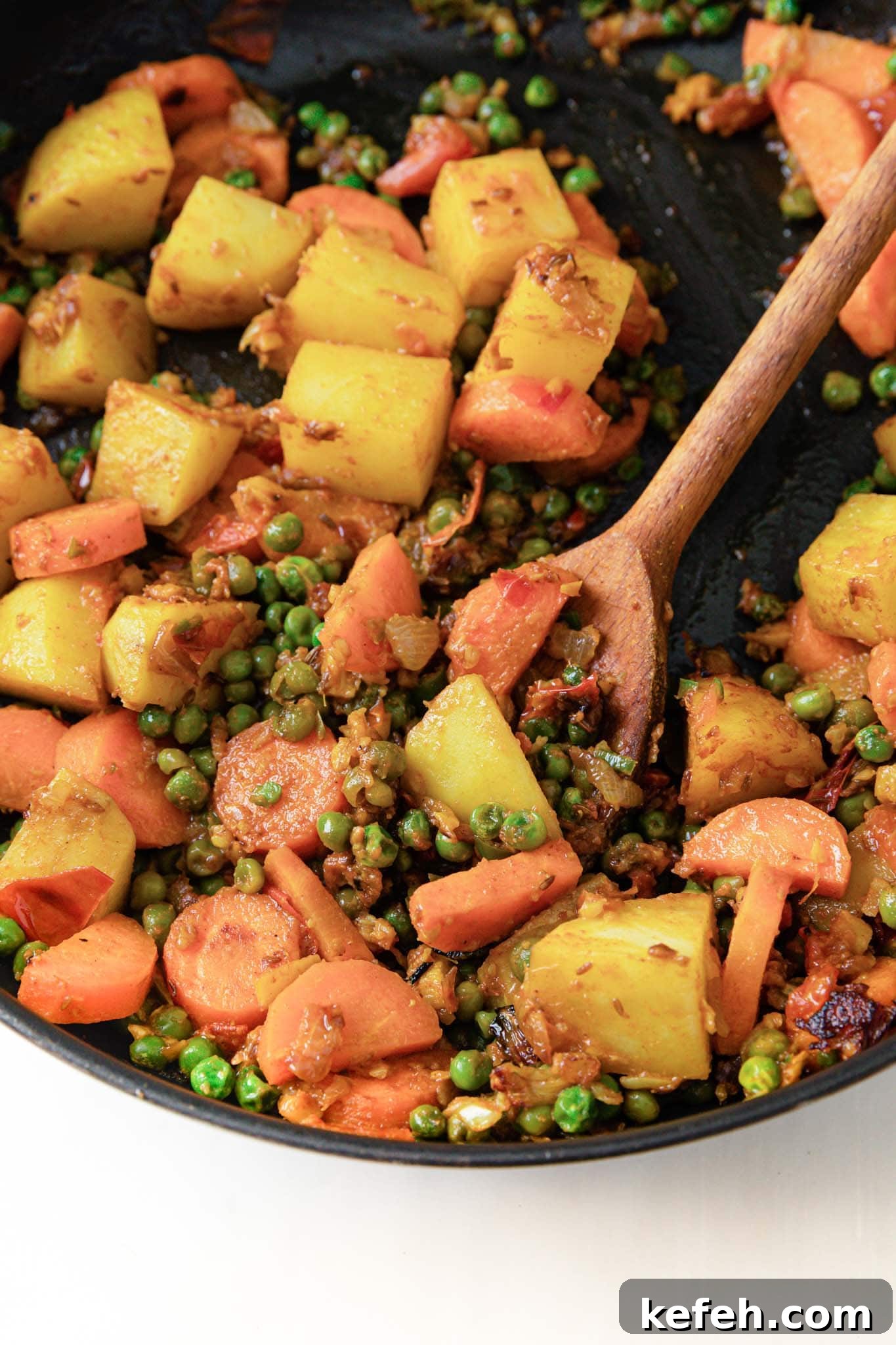 Mixed Vegetable Curry Recipe: Flavorful Indian Veggie Stew 6 Potatoes, carrots, and peas in a black pan with a wooden spoon