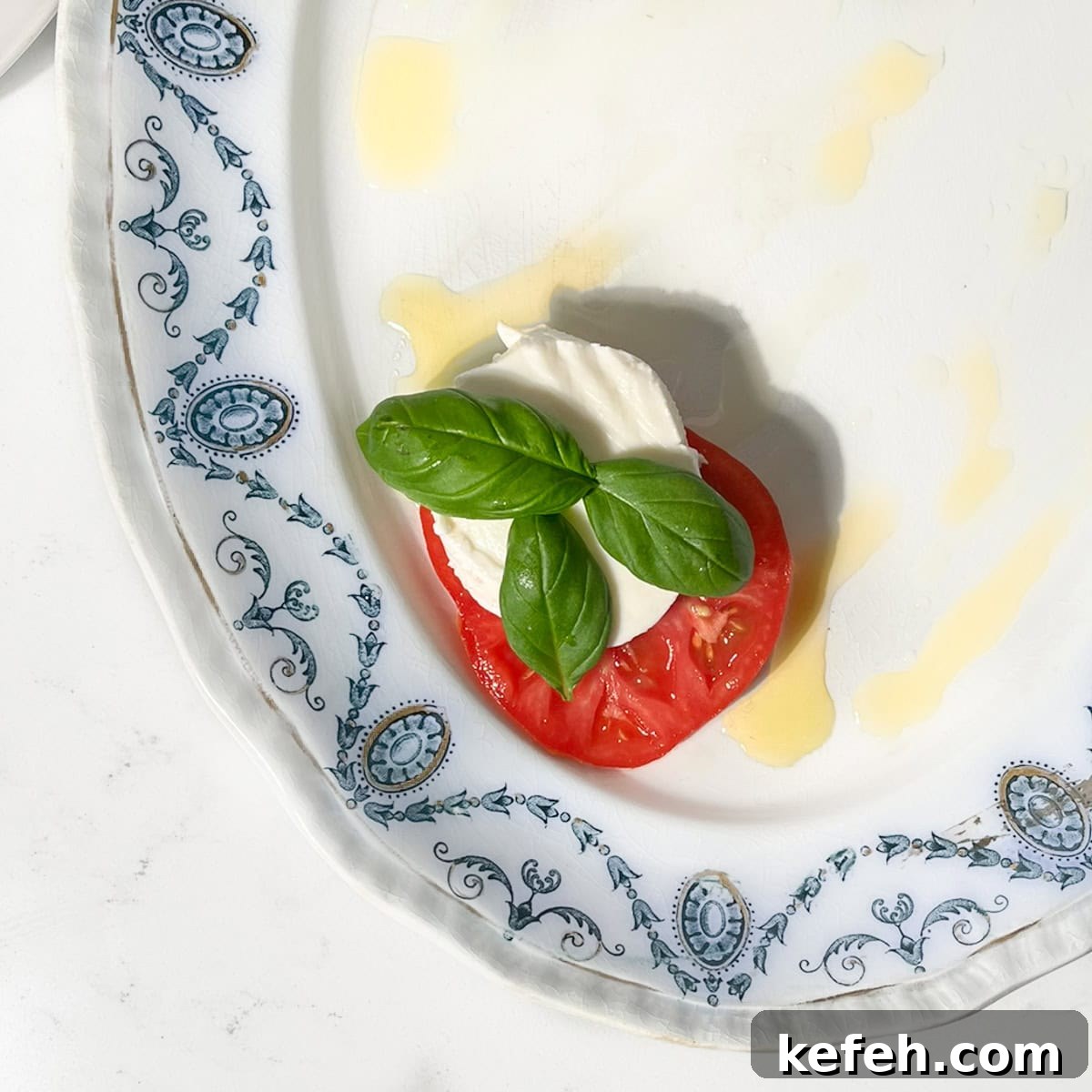 One slice of tomato with a slice of mozzarella and some basil leaves on a plate.