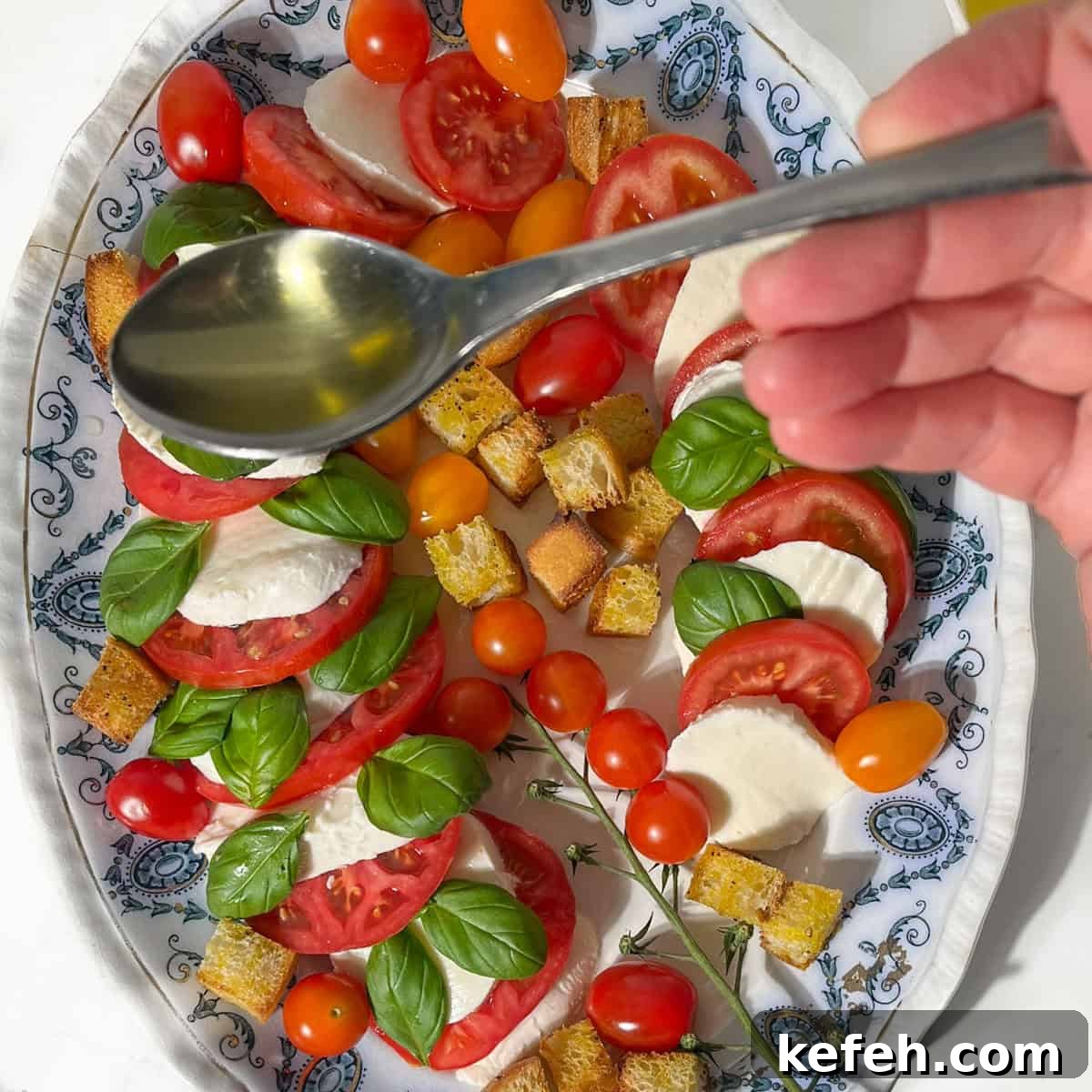 Drizzling olive oil over a caprese salad on an oval plate.