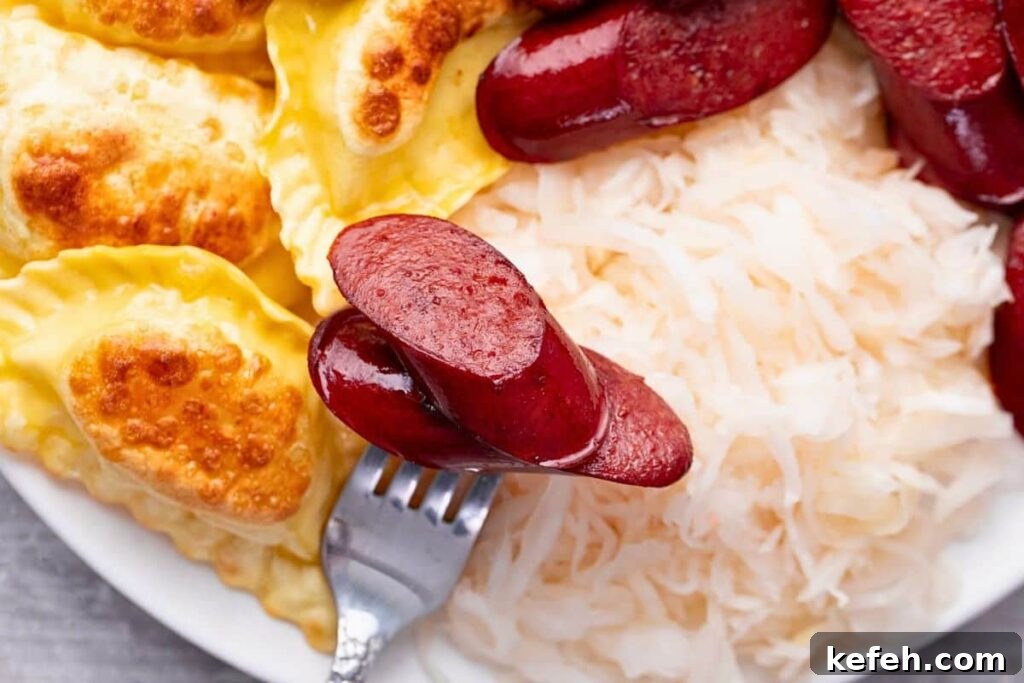 Crispy Juicy Air Fryer Kielbasa Recipe That Melts in Your Mouth 9 closeup view of a fork with kielbasa on the end laying over sauerkraut and pierogies