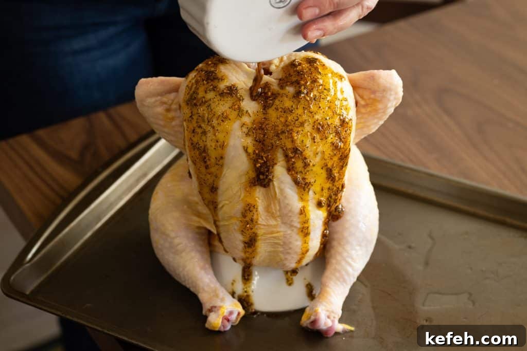 Olive oil and chicken seasoning being poured over a whole chicken on a chicken roaster.
