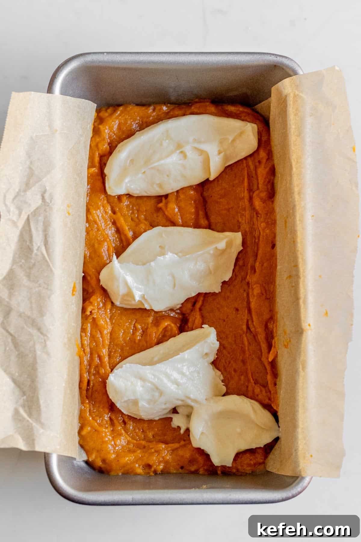 dollops of cream cheese on top of pumpkin bread batter in a loaf pan