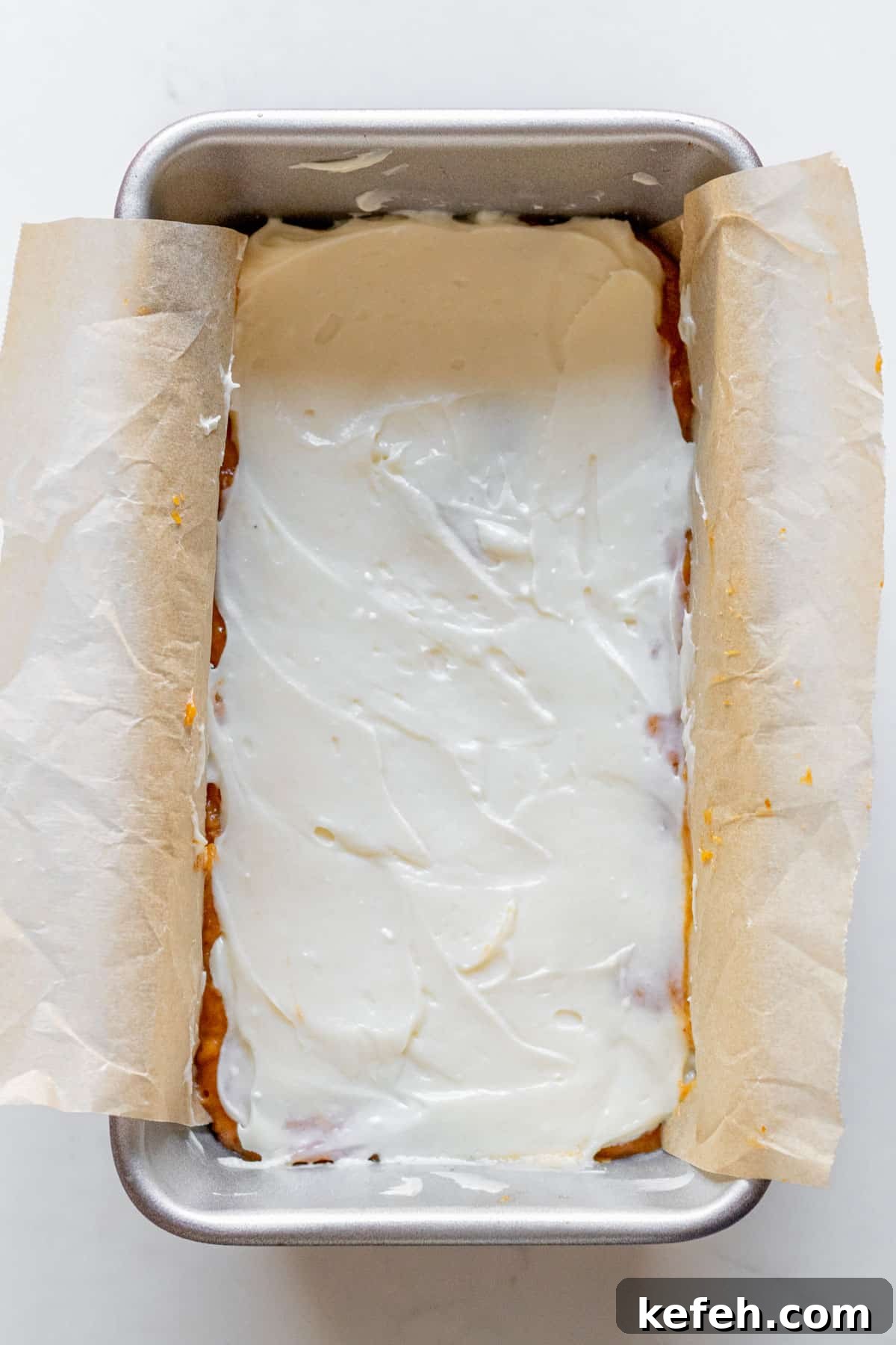 cream cheese spread over pumpkin bread batter in a loaft pan