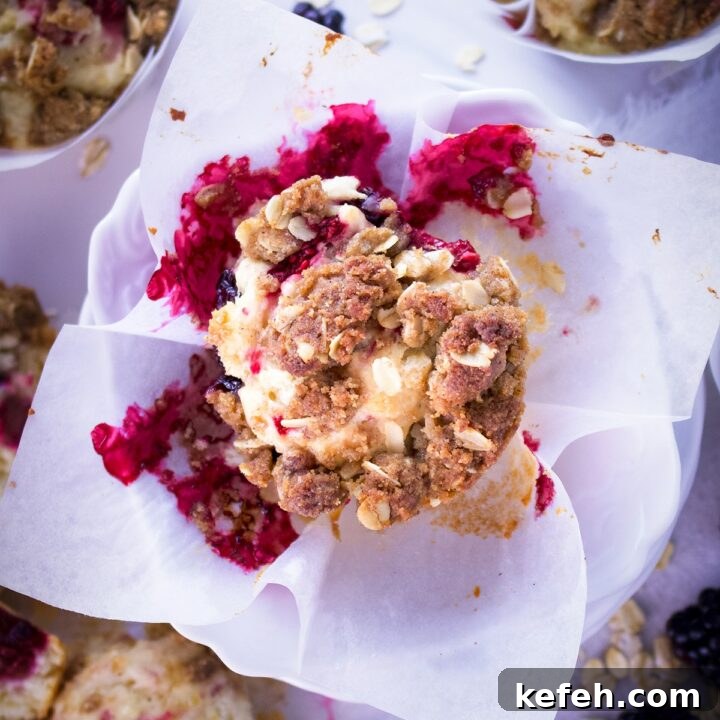 A mixed berry muffin with brown sugar and oats streusel in the center of a table covered in muffins and berries.