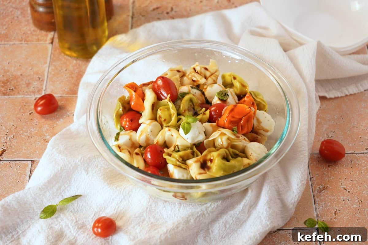 Caprese Tortellini Pasta Salad with Cherry Tomatoes & Basil 2 Tortellini Caprese Pasta Salad in glass bowl with cherry tomatoes scattered around