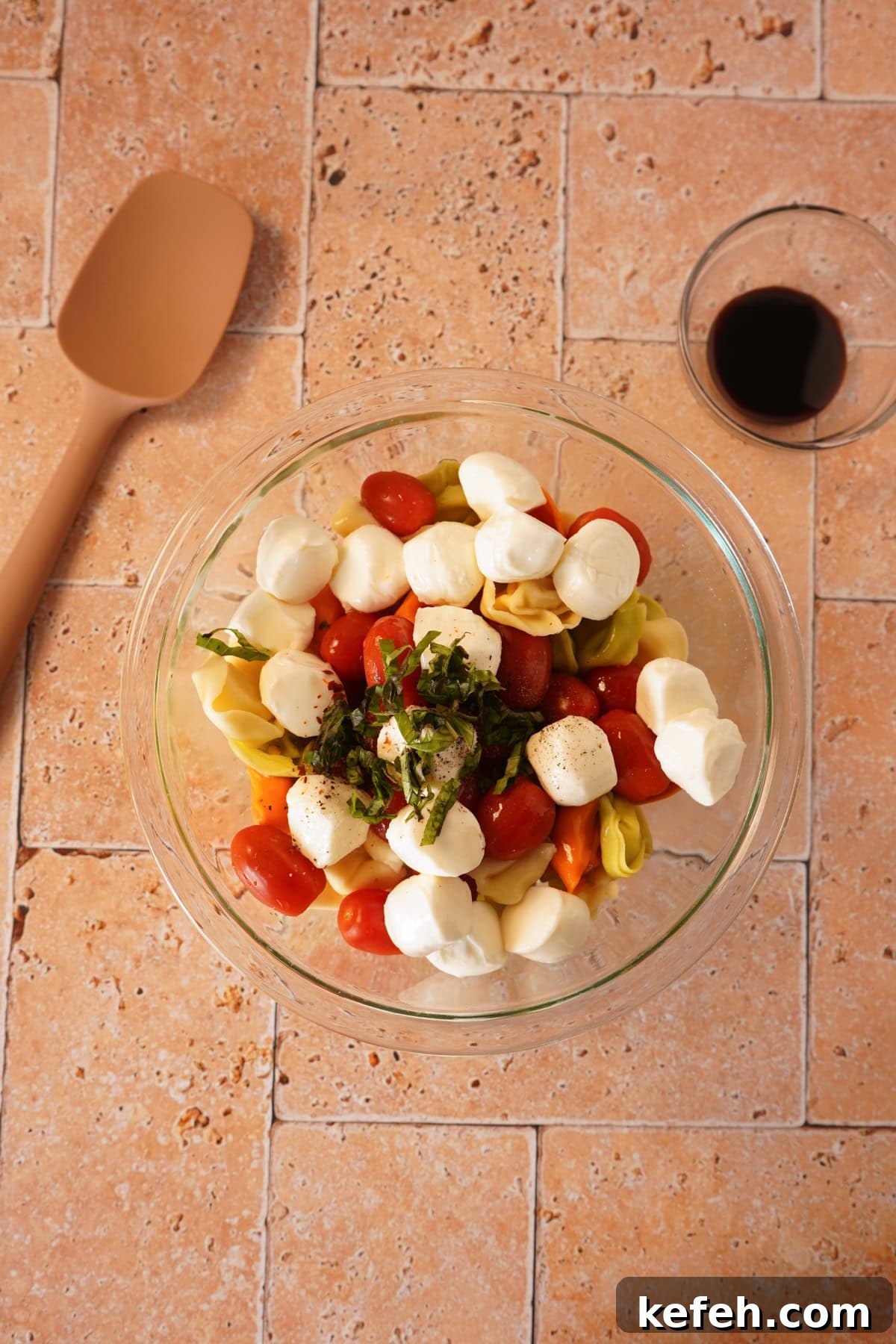 Caprese Tortellini Pasta Salad with Cherry Tomatoes & Basil 5 tortellini, tomatoes, mozzarella, and basil in glass bowl.