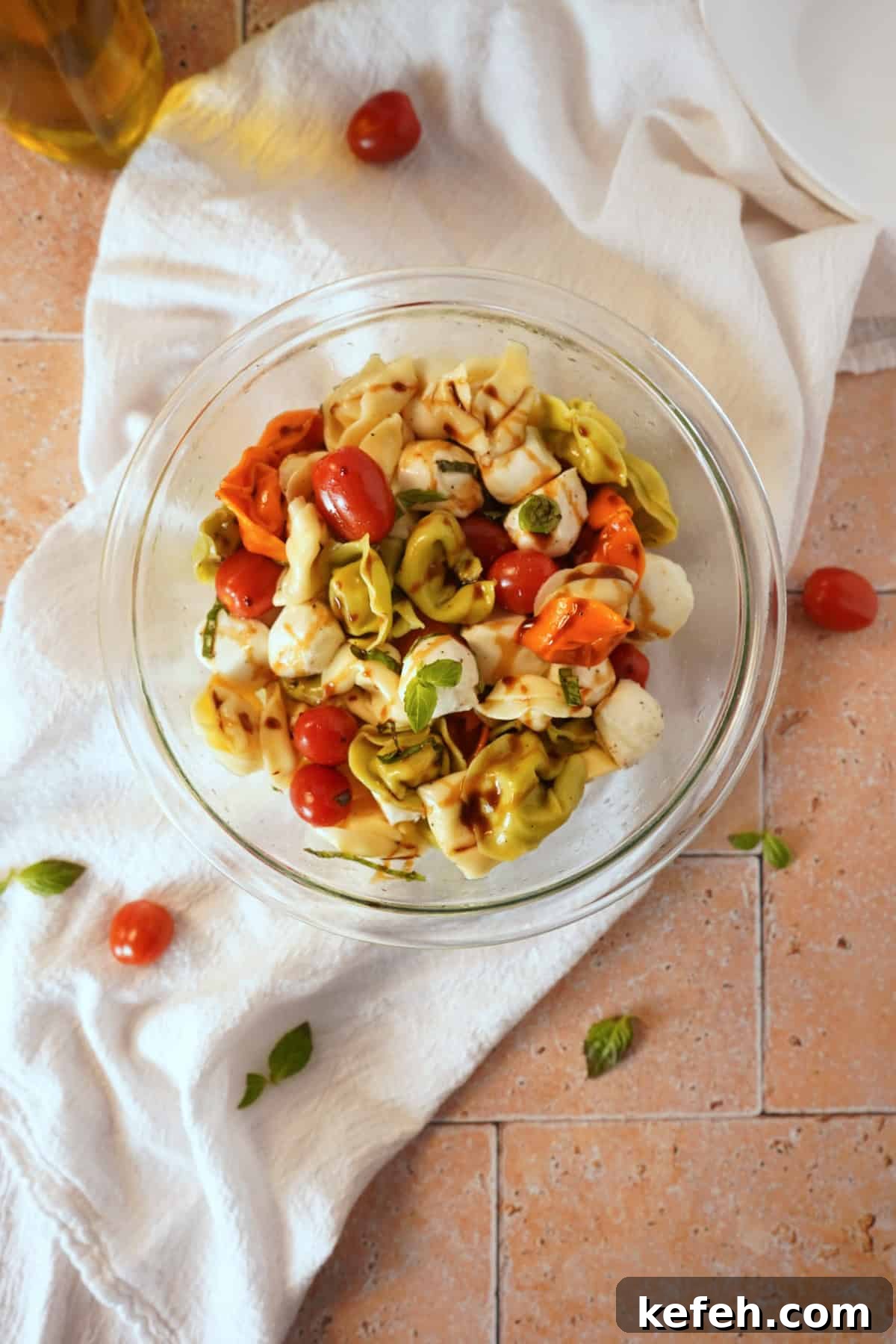 Caprese Tortellini Pasta Salad with Cherry Tomatoes & Basil 6 Tortellini pasta salad in bowl on white linen with balsamic glaze.