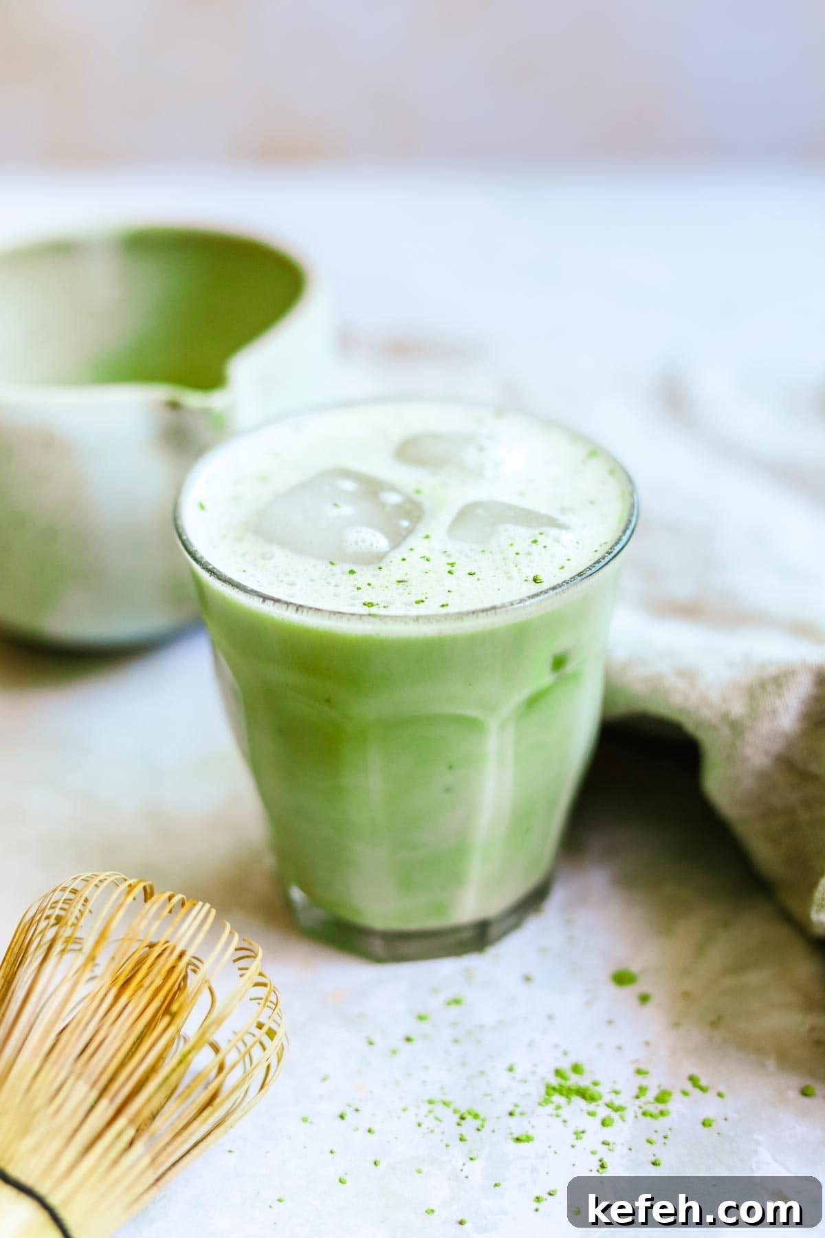 Vanilla matcha latte in a Duralex glass with ice and oat milk foam.