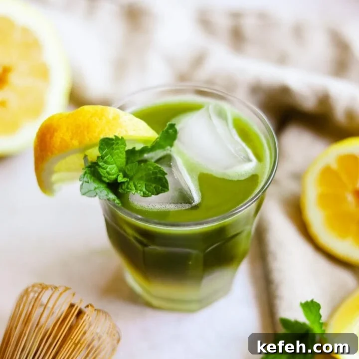 Green tea matcha lemonade in a glass with a lemon wedge and sprig of mint.