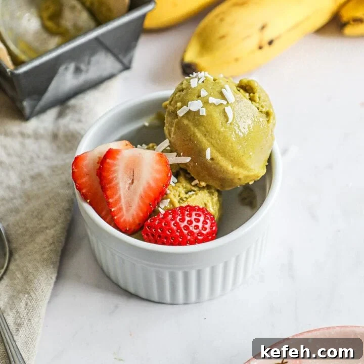 Vegan matcha banana ice cream in a small ramekin with strawberries and coconut flakes as garnish.
