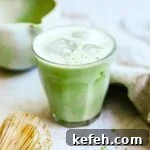 Vanilla matcha latte in a Duralex glass with ice and oat milk foam.