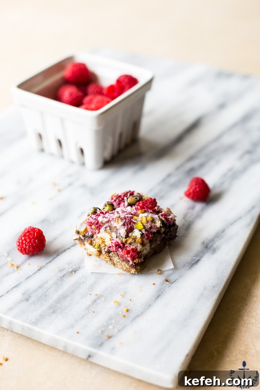 Photo of one raspberry pistachio bar on a marble board with container of raspberries
