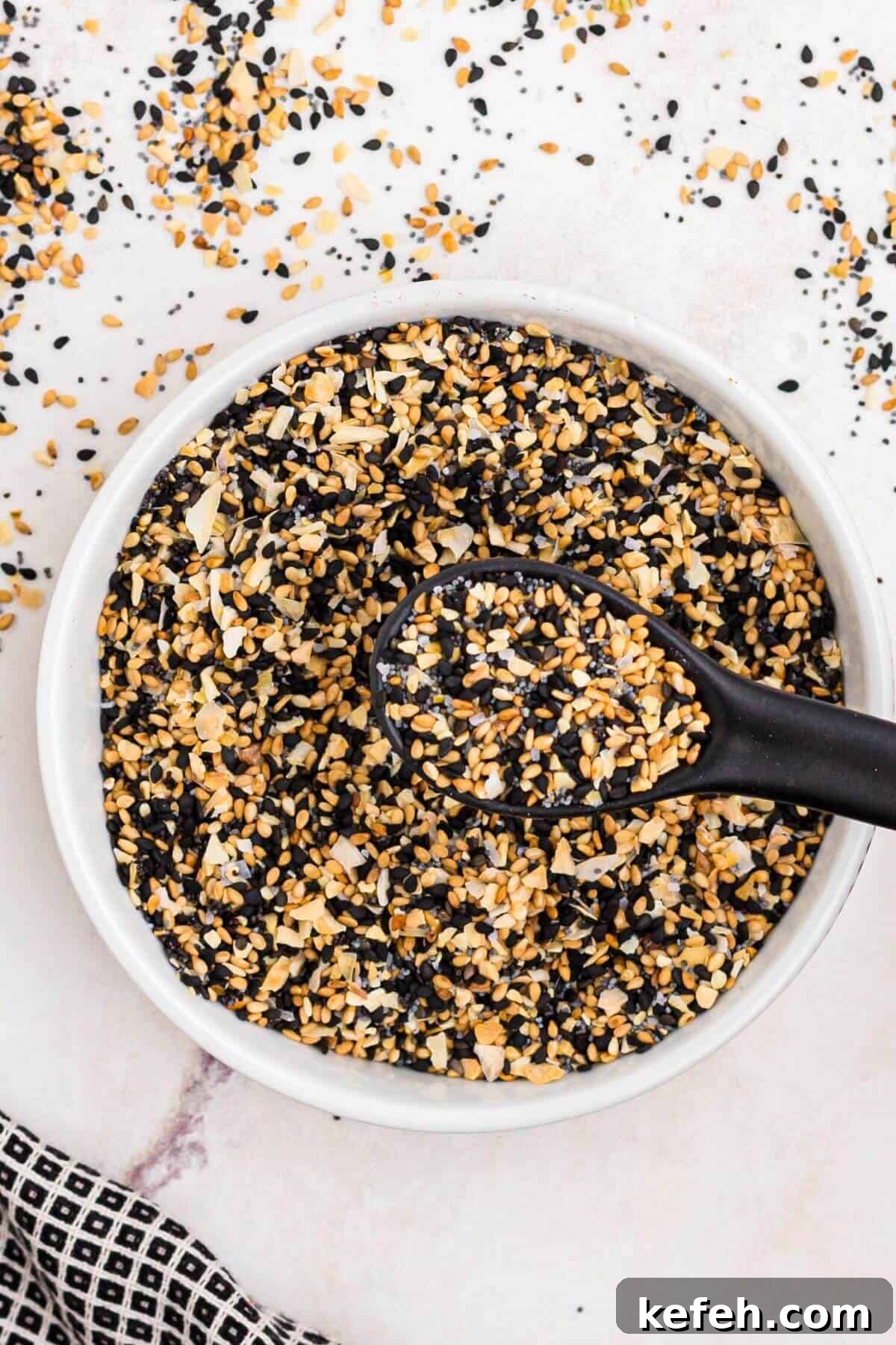 Seeds and seasonings in a small white bowl with a black spoon in the bowl.