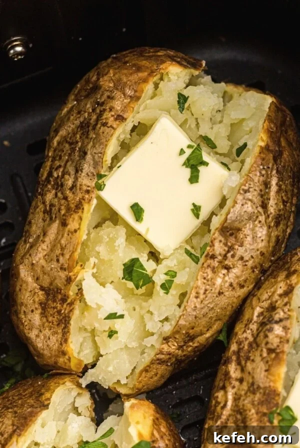 Golden baked potatoes in the air fryer basket after being cooked with butter and parsley flakes