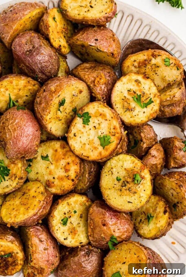 Golden crispy seasoned baby potatoes on a white plate with a serving spoon in the corner of the plate.