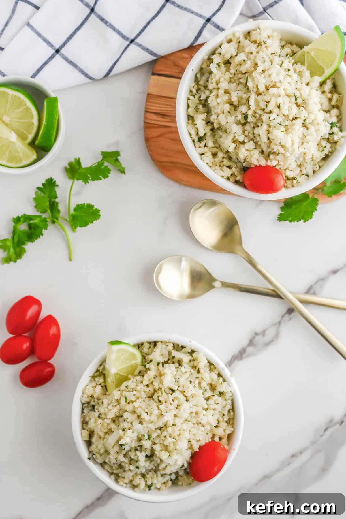 Cilantro Lime Cauliflower Rice Recipe for Flavorful Low-Carb Sides 4 Two bowls of cilantro lime cauliflower rice garnished with lime wedges and cherry tomatoes, accompanied by gold spoons on a marble countertop.