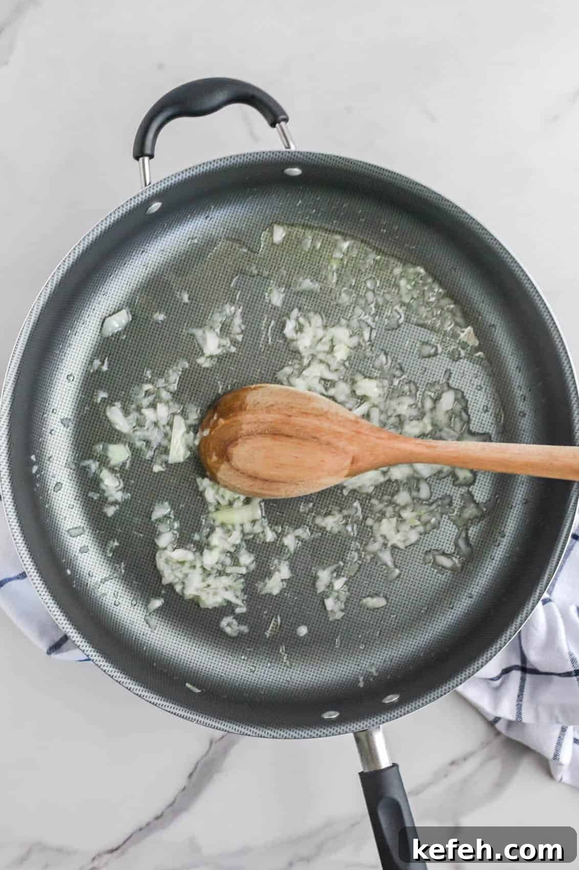 Cilantro Lime Cauliflower Rice Recipe for Flavorful Low-Carb Sides 5 A non-stick frying pan on a white surface containing chopped garlic, cilantro, and oil, with a wooden spoon mixing the ingredients.