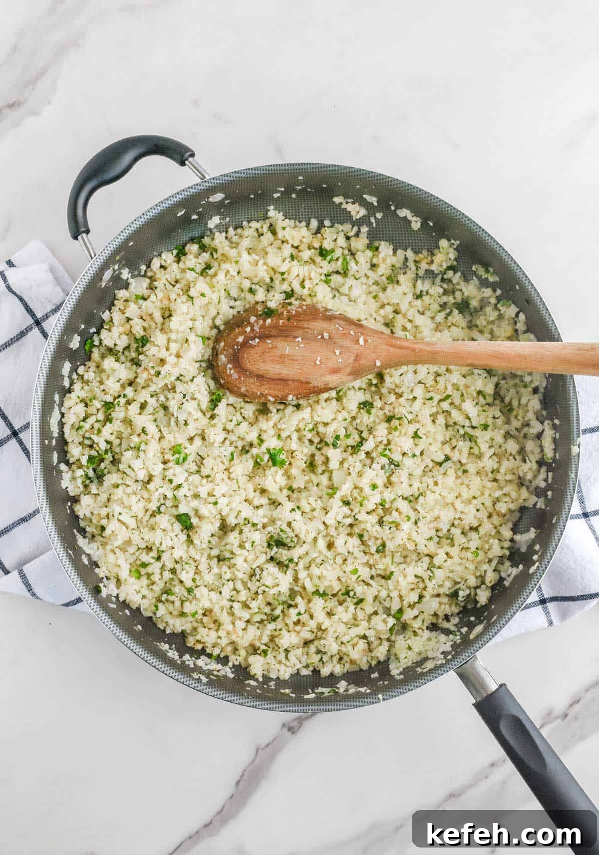 Cilantro Lime Cauliflower Rice Recipe for Flavorful Low-Carb Sides 8 Cilantro cauliflower lime rice in a frying pan with a wooden spoon.
