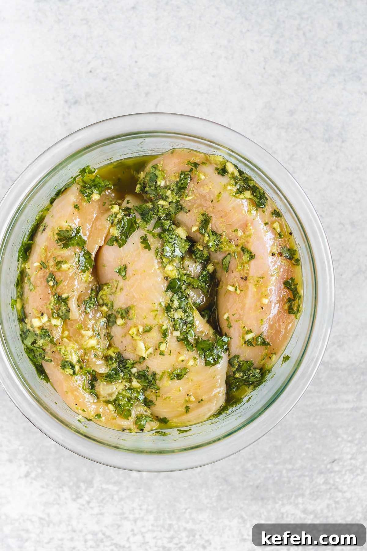 Raw chicken breasts sitting in a cilantro lime marinade in a glass bowl.
