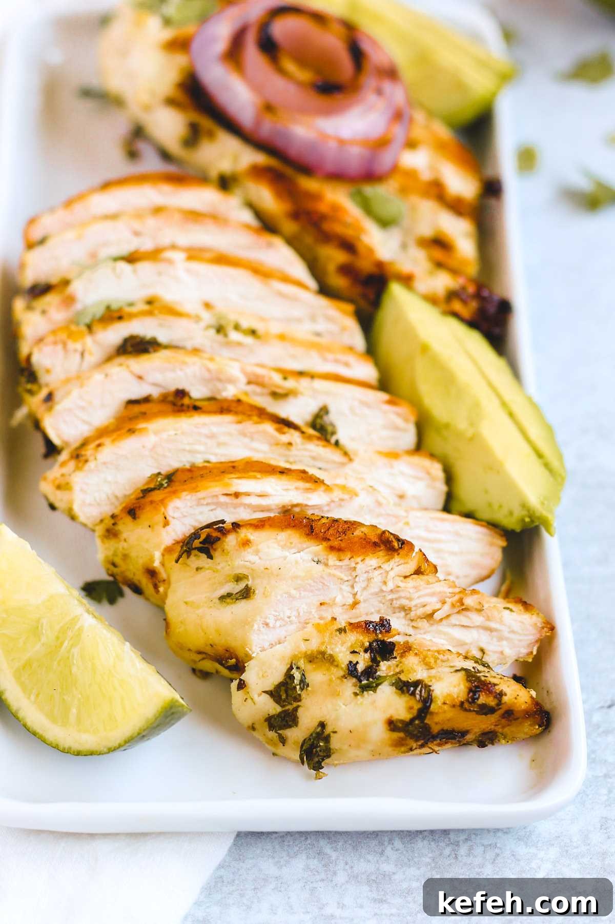 Cooked, and sliced, cilantro lime chicken breast on a rectangular plate with lime wedge and sliced avocado on the side.