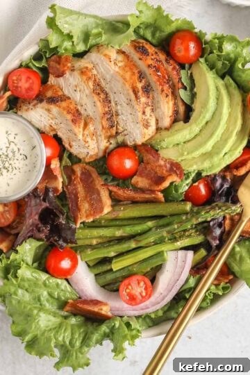 Salad bowl filled with a BLT salad with chicken, avocado, asparagus, and a side of ranch.