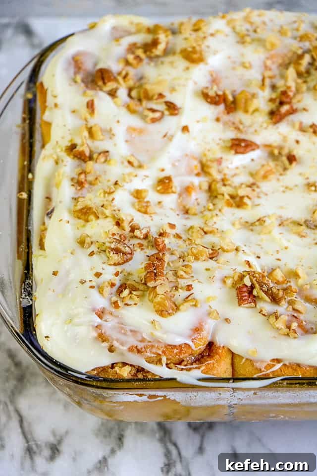 pan of pumpkin cinnamon rolls with a cream cheese frosting in a glass pan on a marble background