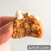 A hand holding a peanut butter cookie fat bomb with a bite out of it.