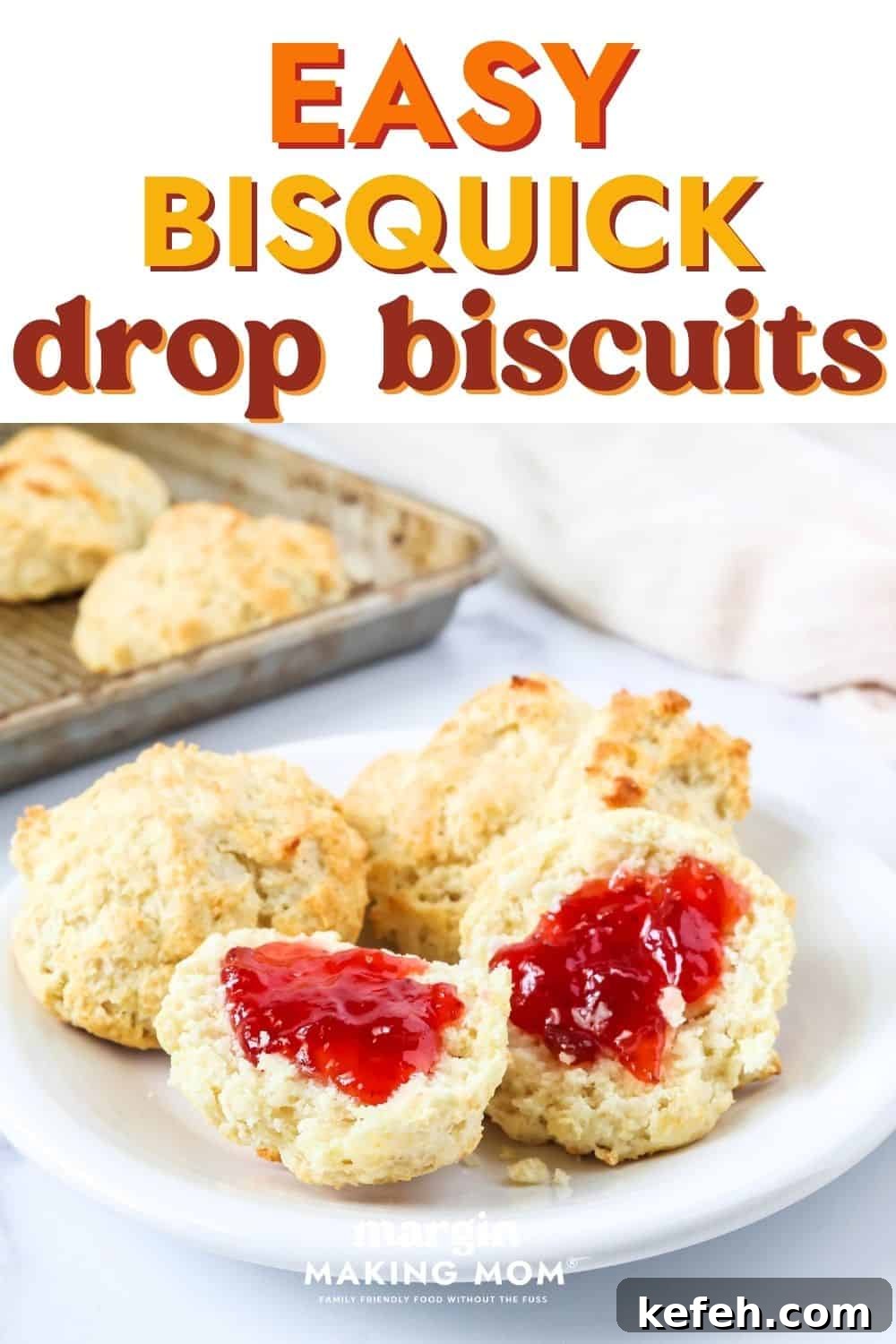 Easy Bisquick drop biscuits served on a white plate, with the pan of biscuits in the background. One of the biscuits is halved and spread with strawberry jam.