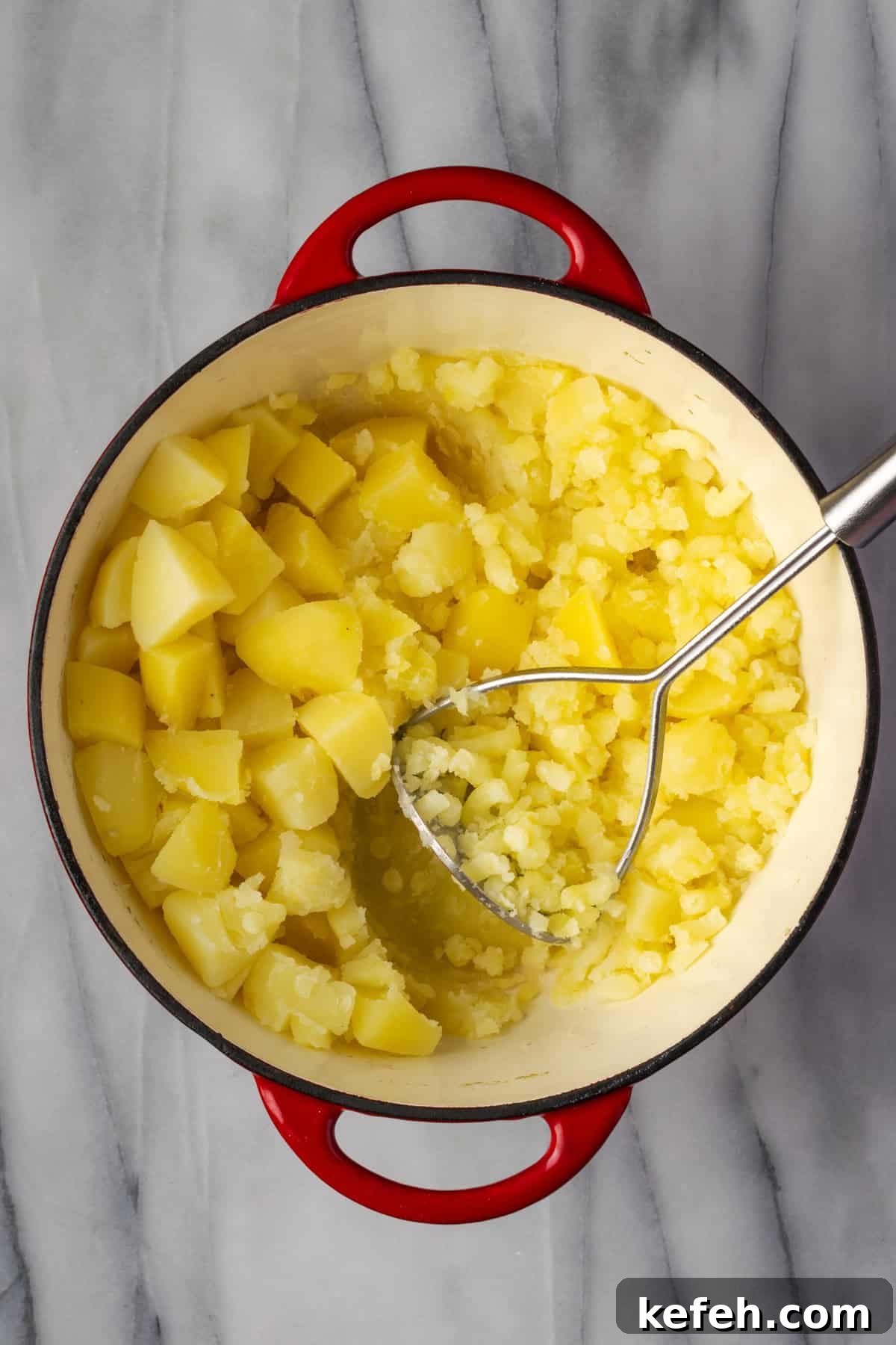 Cooked potatoes being mashed in a large pot.