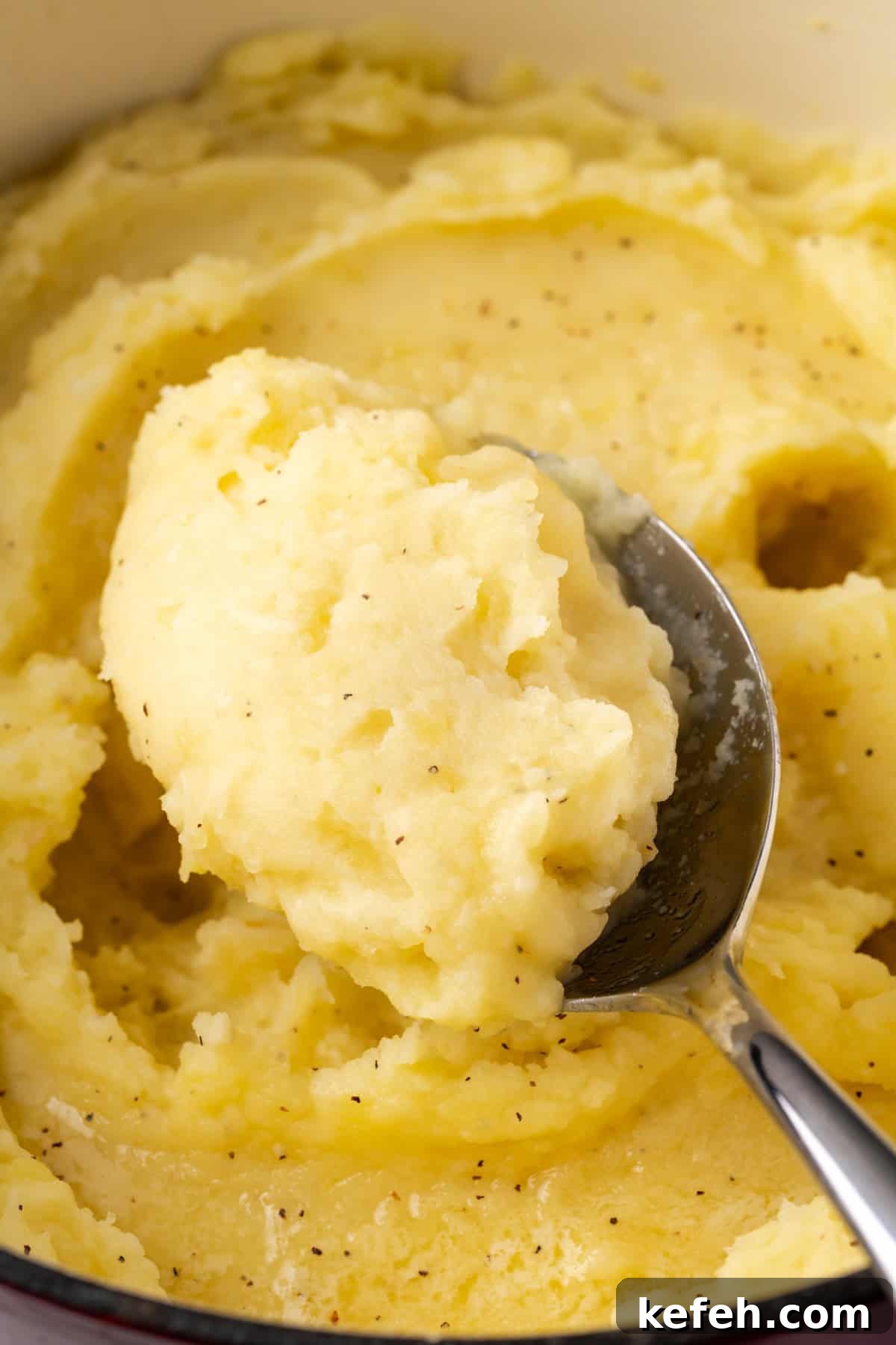 A spoon scooping gluten free mashed potatoes from a large pot.