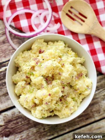 White bowl of Potato Salad sitting on a wooden table.