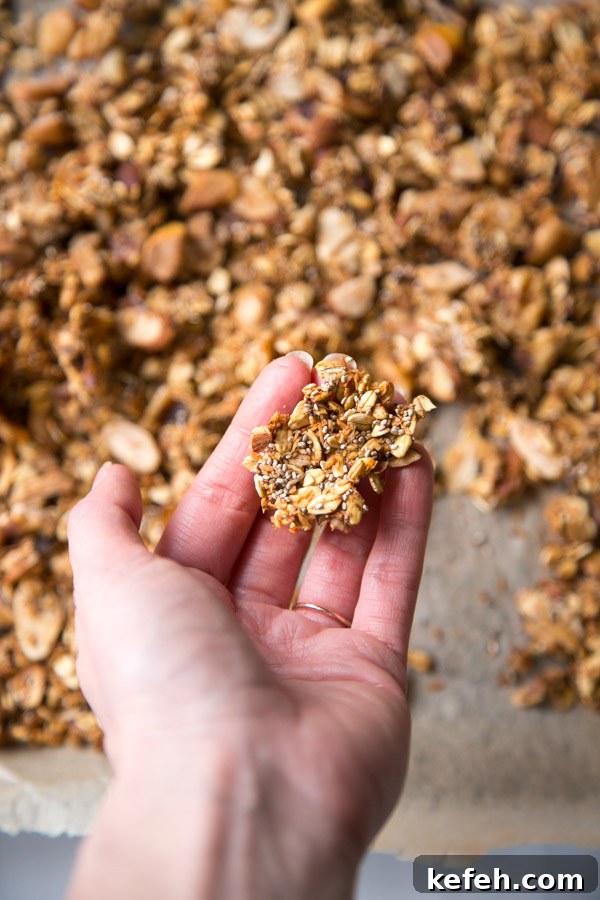 hand holding a cluster of sugarless granola over a sheet pan