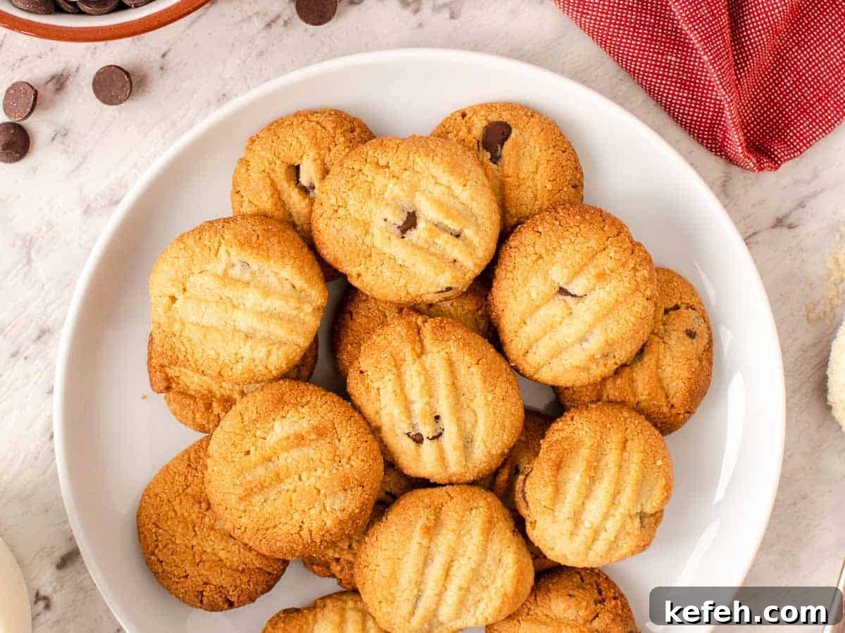 Crispy Almond Flour Cookies: Simple Gluten-Free Treats 5 The cookies on a white plate with chocolate chips and almonds scattered nearby viewed from above.