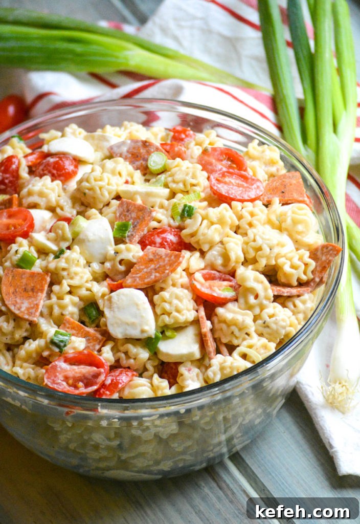 a quick and easy pasta salad with pepperoni shown in a large glass bowl with a wooden spoon on the side