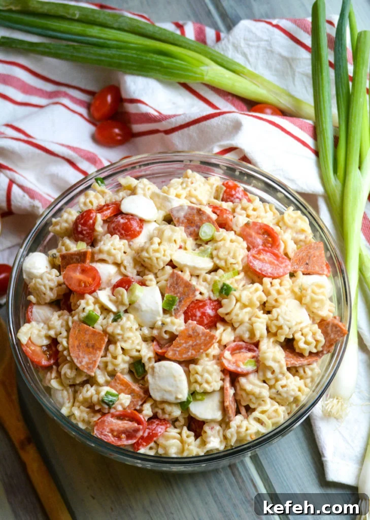 a quick and easy pasta salad with pepperoni shown in a large glass bowl with a wooden spoon on the side