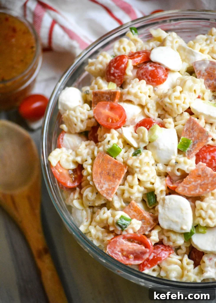 a quick and easy pasta salad with pepperoni shown in a large glass bowl with a wooden spoon on the side