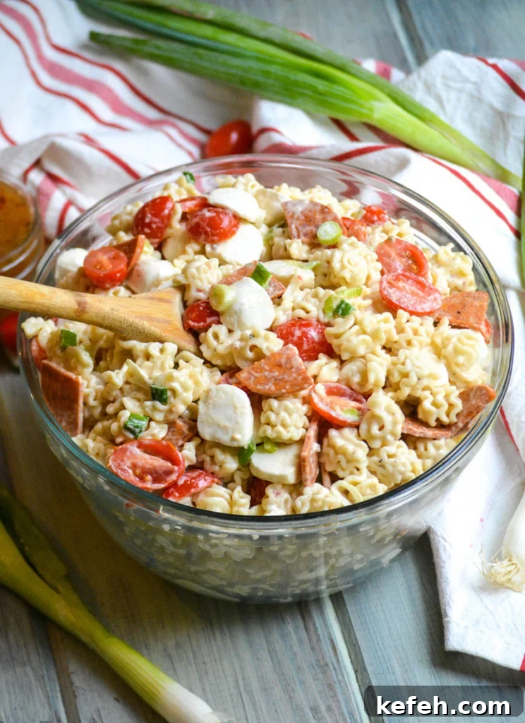 a quick and easy pasta salad with pepperoni shown in a large glass bowl with a wooden spoon on the side