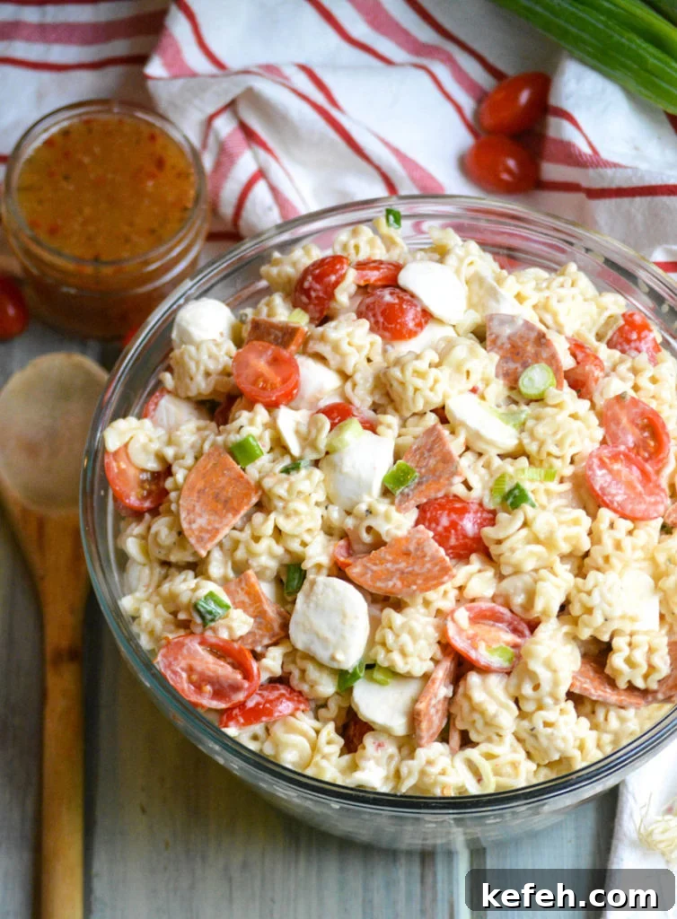 a quick and easy pasta salad with pepperoni shown in a large glass bowl with a wooden spoon on the side