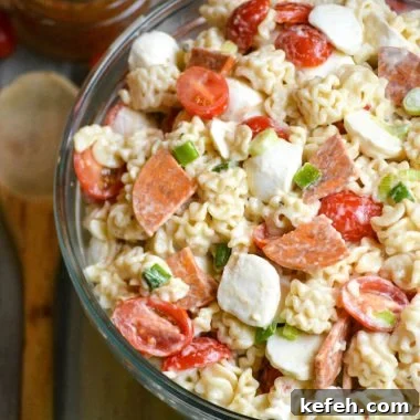 a quick and easy pasta salad with pepperoni shown in a large glass bowl with a wooden spoon on the side